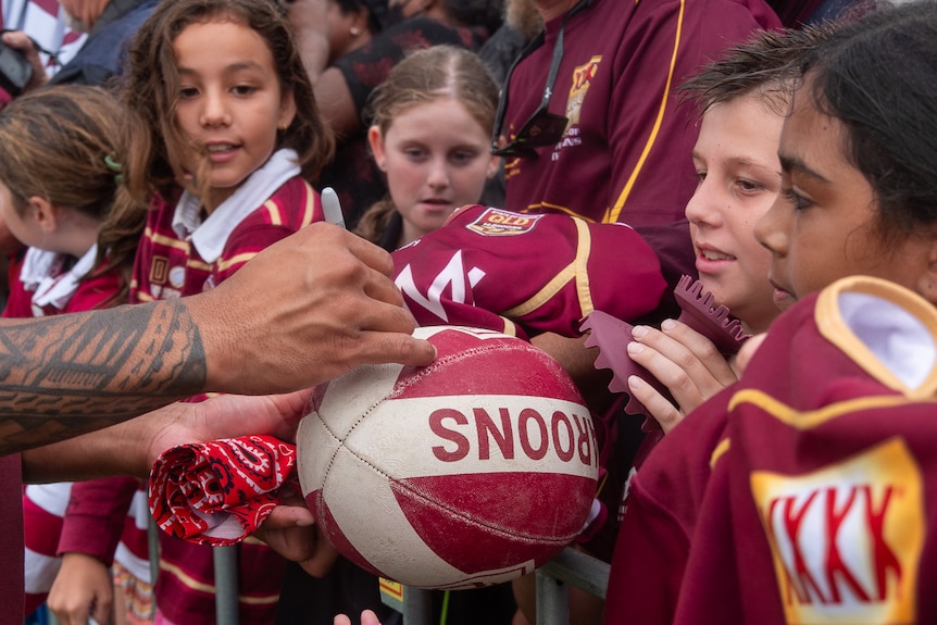 football being signed by player with young maroons fans in background