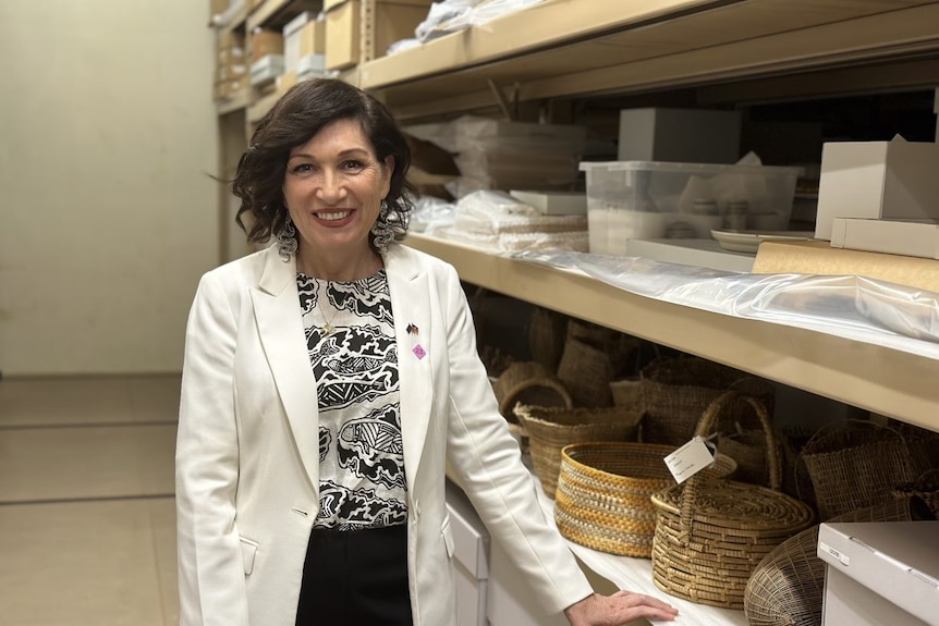 Leeanne Enoch wearing a white jacket standing next to shelves carrying items.
