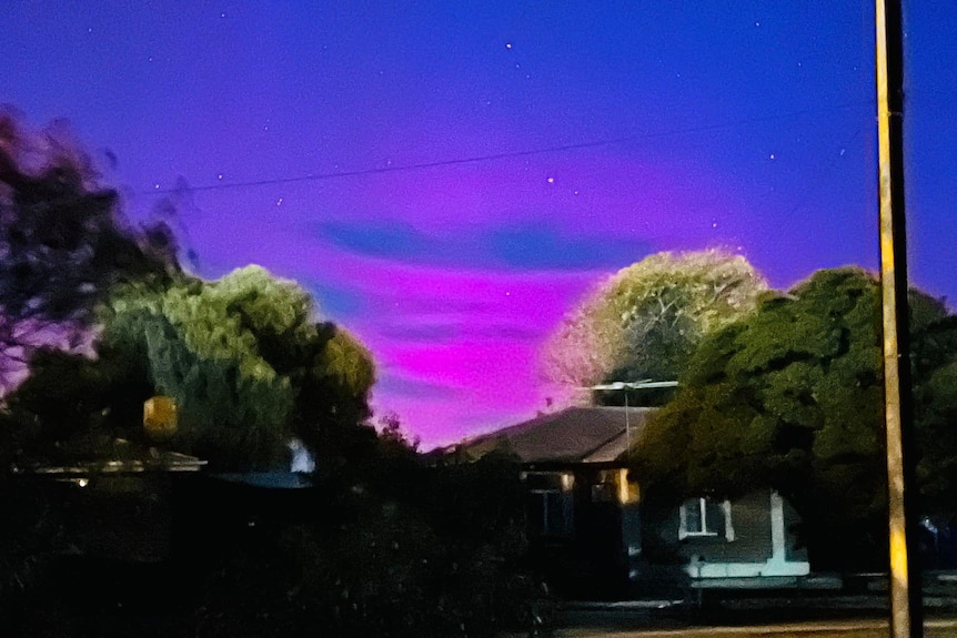 Pink and purple sky is seen about the roofline of a house