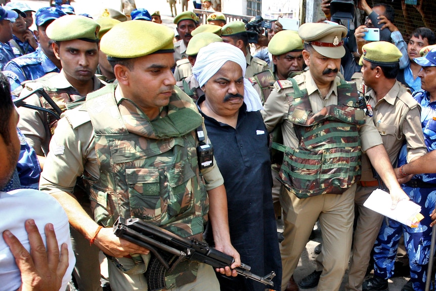 Armed police officers in India escort an older man.
