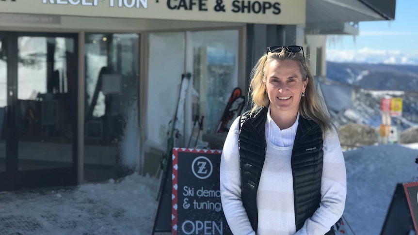 A woman stands in front of a business situated in a snowy alpine area.