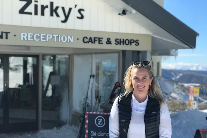 A woman stands in front of a business situated in a snowy alpine area.