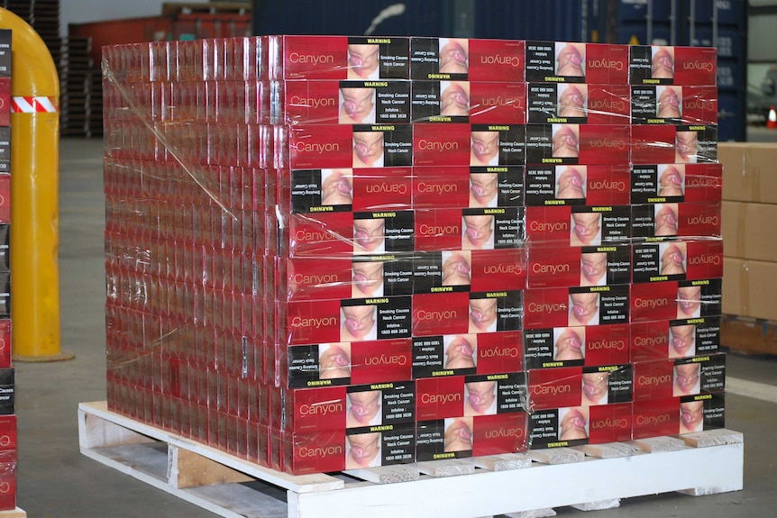A pallet sits on the ground stacked with red boxes of illicit cigarettes.