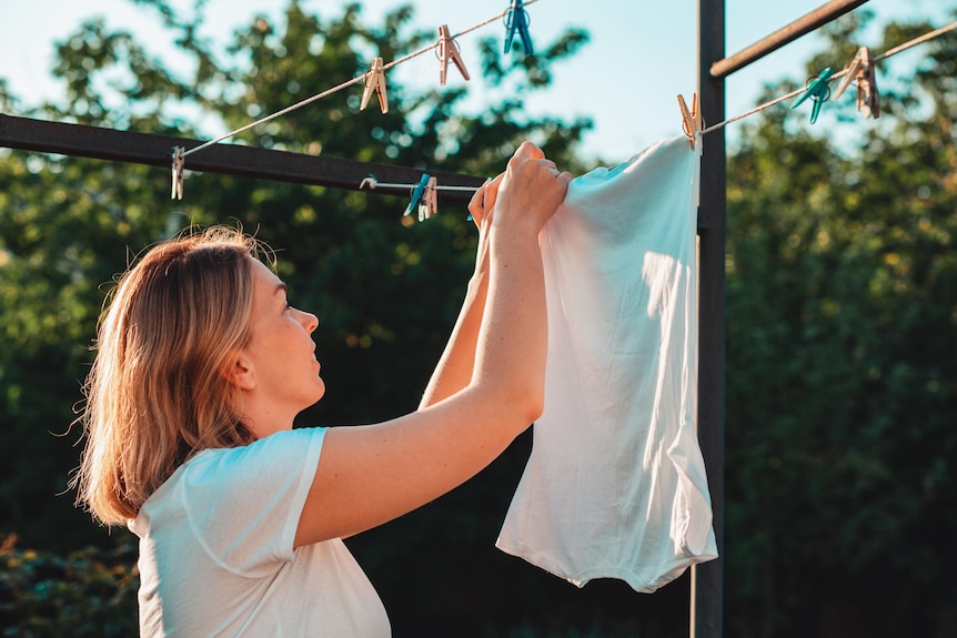 A woman in her thirties with short blonde hair hangs a white shirt on a clothesline.