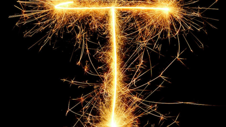 Close-Up Of Firework Display Against Black Background. The fireworks look like sparklers in the shape of a capital T. 