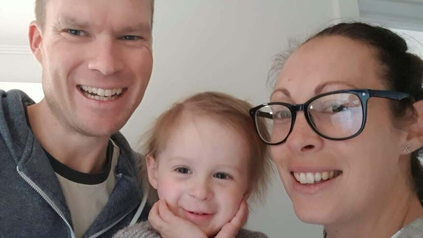 A mother and father pose for a selfie with their toddler daughter