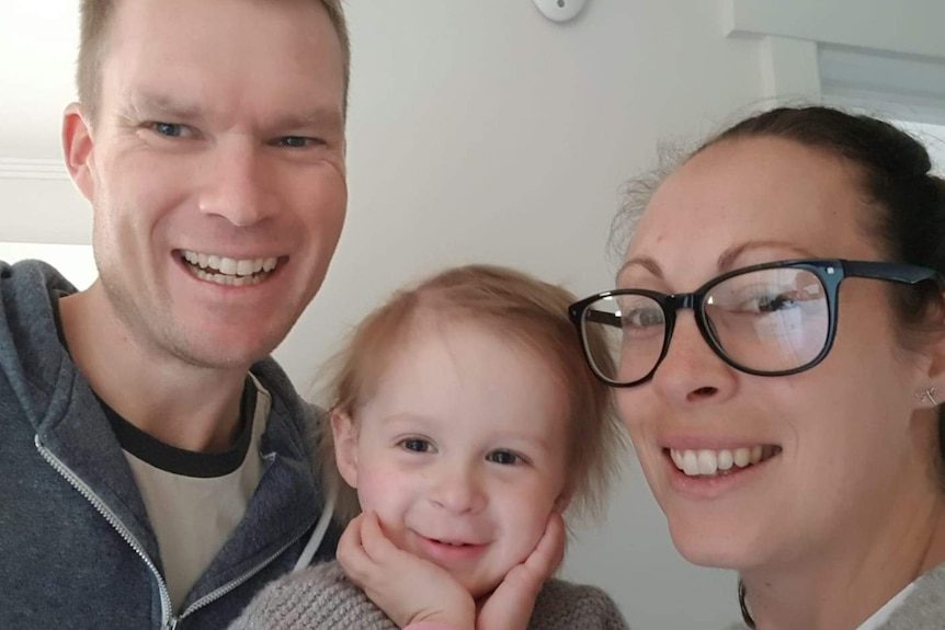 A mother and father pose for a selfie with their toddler daughter