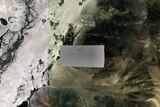 A satellite photo of a region in Tibet shows a grey pixelated blur over sandy mountain peaks.
