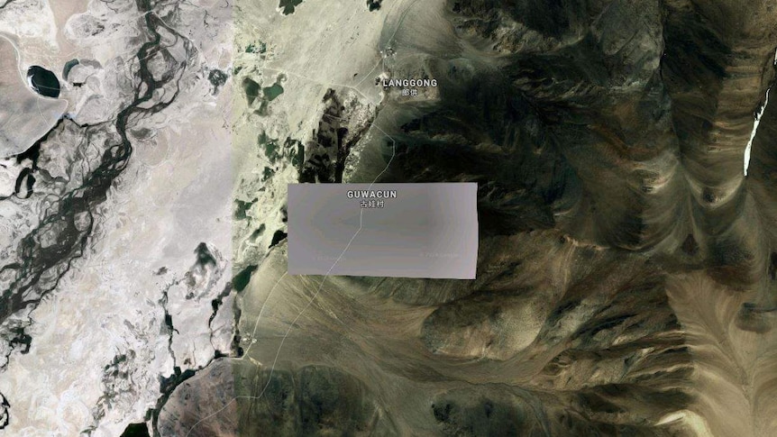 A satellite photo of a region in Tibet shows a grey pixelated blur over sandy mountain peaks.