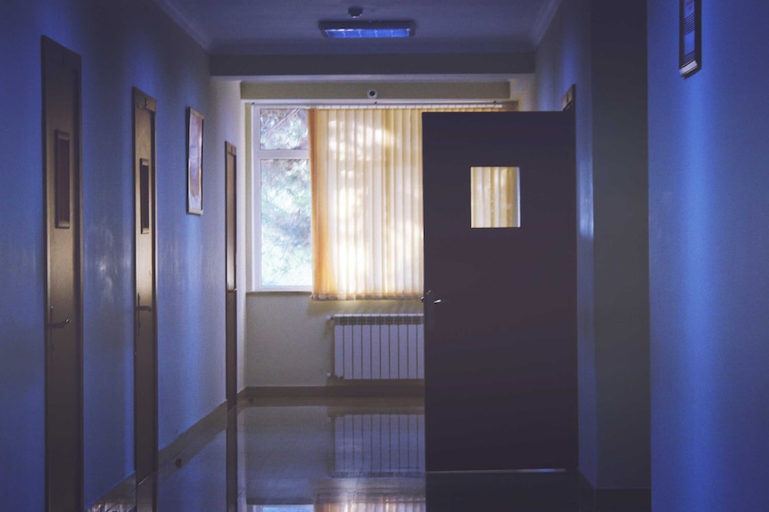 Dimly lit hospital corridor with one door open, a place where listening to and sitting with grief is high demand.