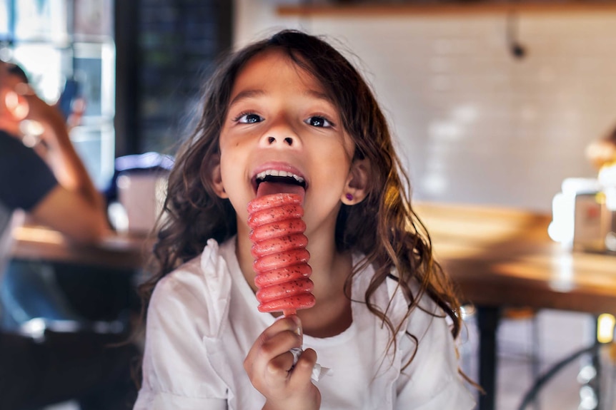 A young girl licks a berry ice block.