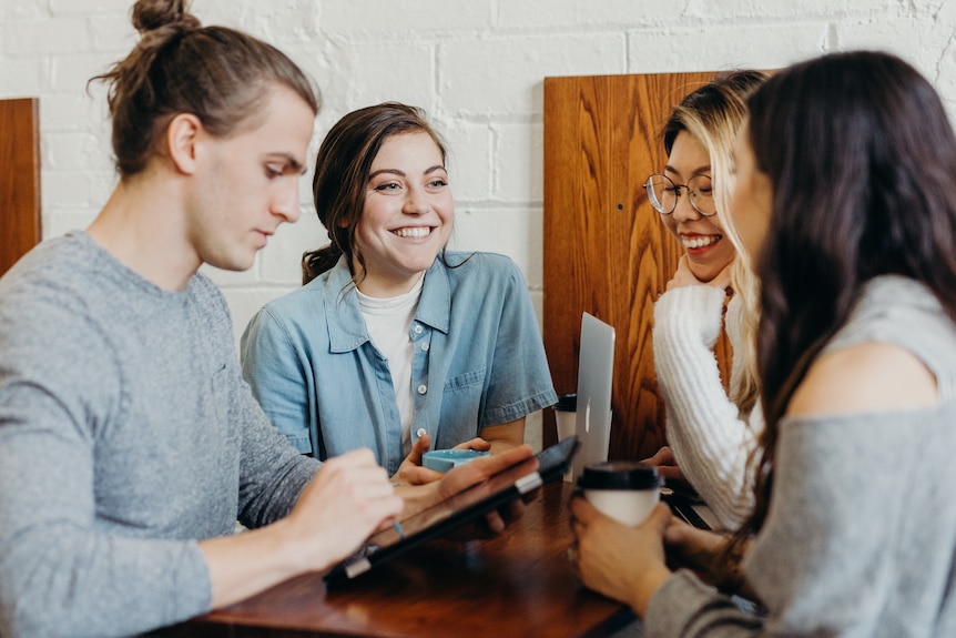 Four work mates sit at a table together and have a good laugh together. 