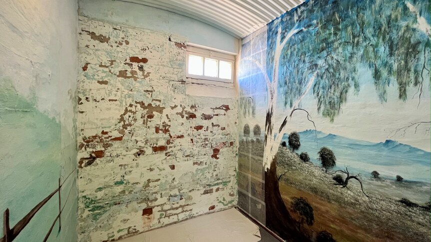 A mural featuring a tree painted on one wall of a very small room. 