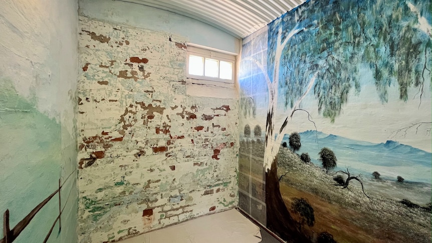 A mural featuring a tree painted on one wall of a very small room. 