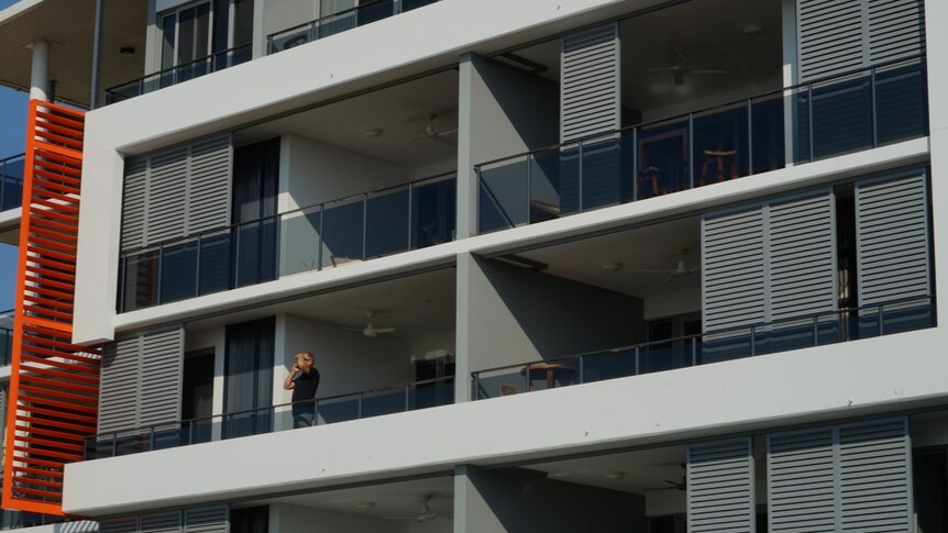 A man stands on an apartment balcony.