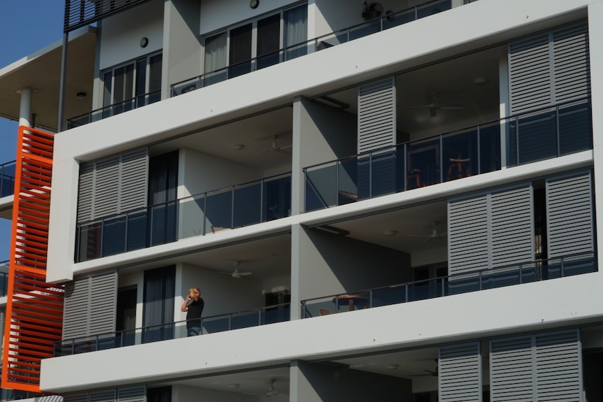 A man stands on an apartment balcony.