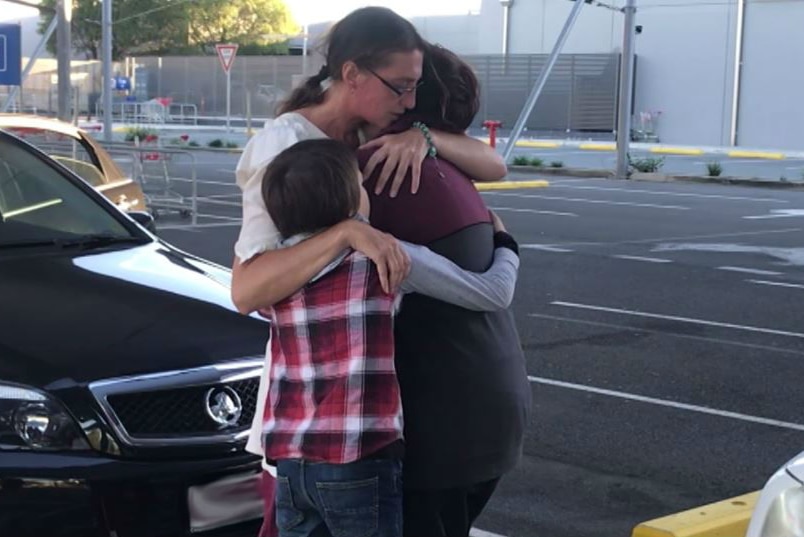 A woman hugs her teenage children tight in a carpark