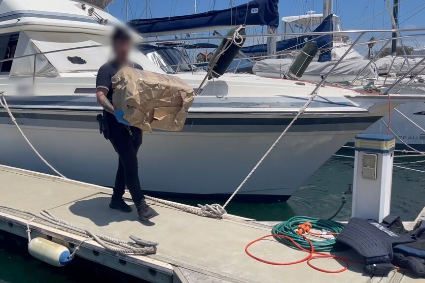 A police officer walking with a large package of drugs off a boat at a marina