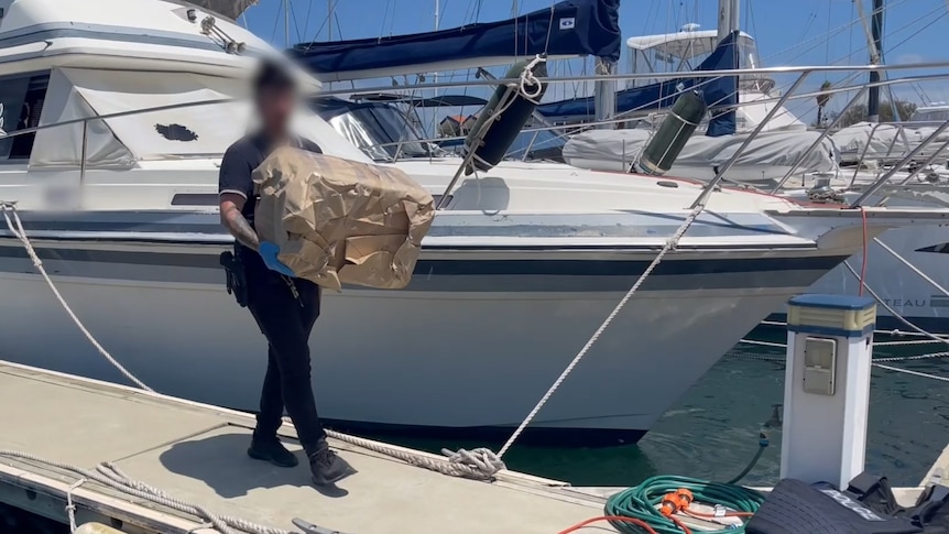 A police officer walking with a large package of drugs off a boat at a marina