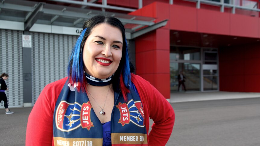 A female jets supporter has her hair coloured red and blue for the Jets, she has red lipstick and is wearing team colours