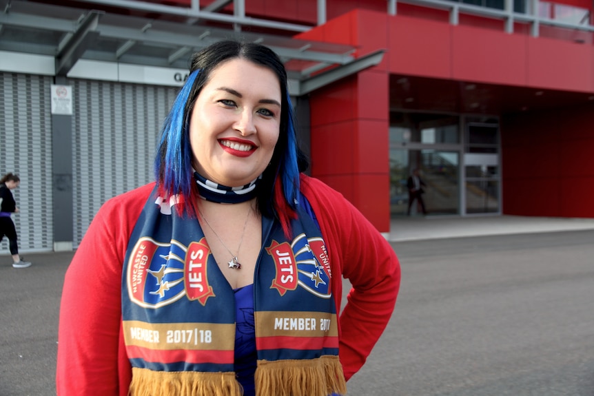 A female jets supporter has her hair coloured red and blue for the Jets, she has red lipstick and is wearing team colours