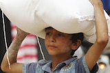 A boy carrying a bag of food on his head in Syria.
