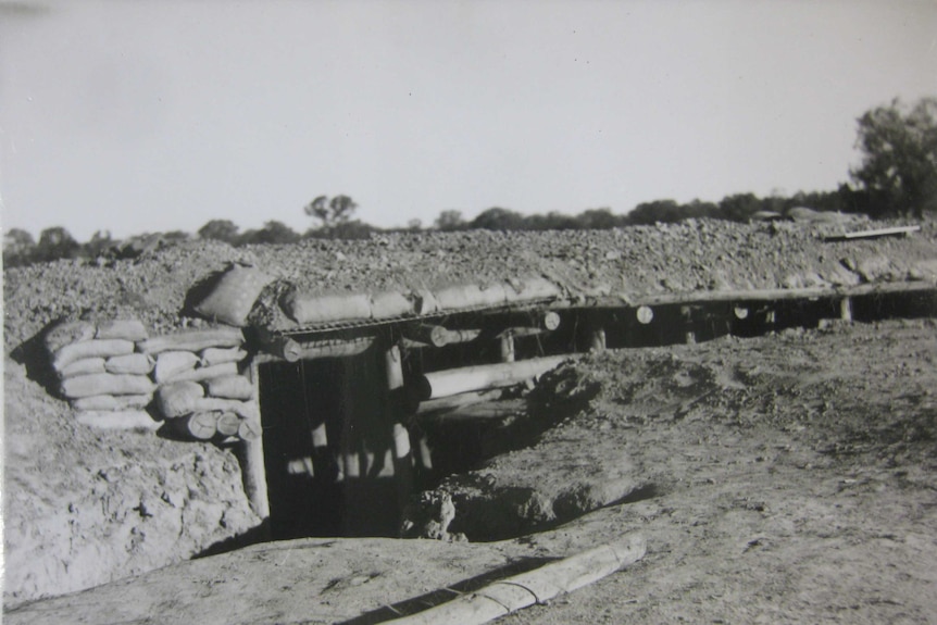 A black and white photograph of a bunker with sand bags at its entrance and a rubble roof.