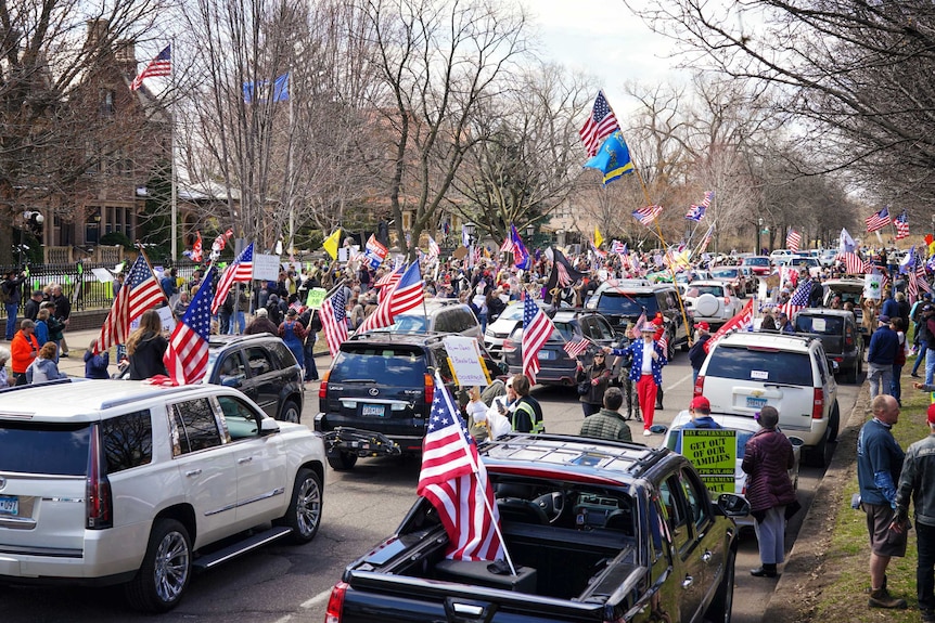 Hundreds of people waving American flags walk outside a house in Minnesota.