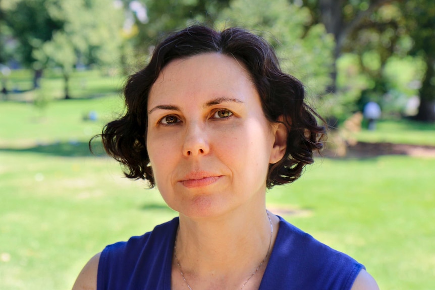 Woman with black, curly hair staring pensively with trees in the background.