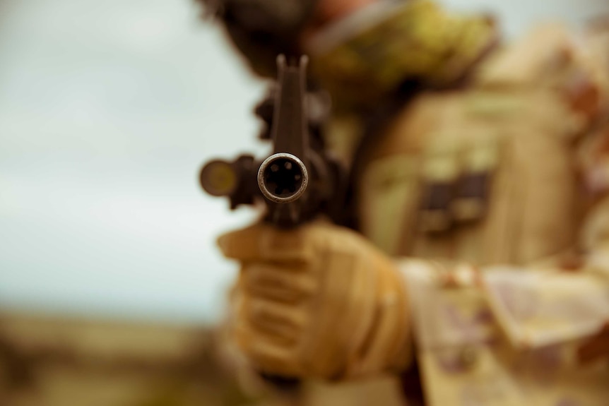 A soldier points a gun down the barrel of the camera