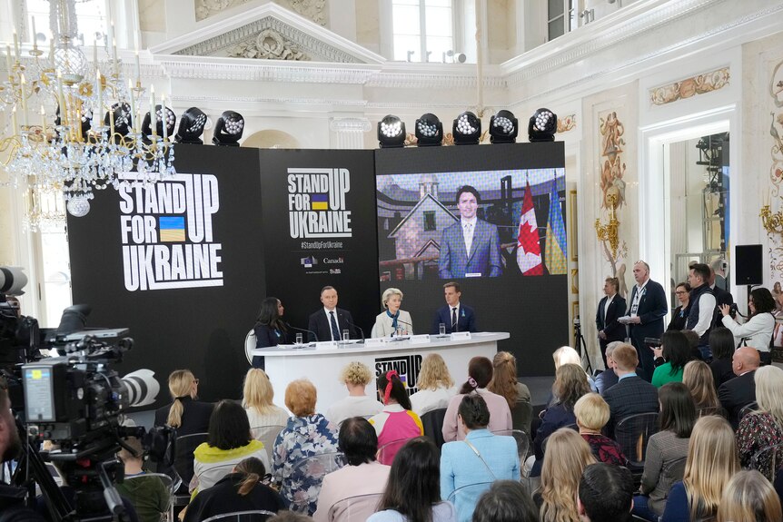 World leaders gather beneath a sign that reads "Stand Up for Ukraine".