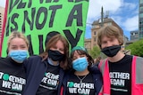 Four young people stand shoulder to shoulder wearing masks and shirts that read 'Together we can'