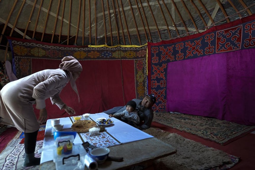 A woman prepares a snack inside a traditional yurt for a man and a child