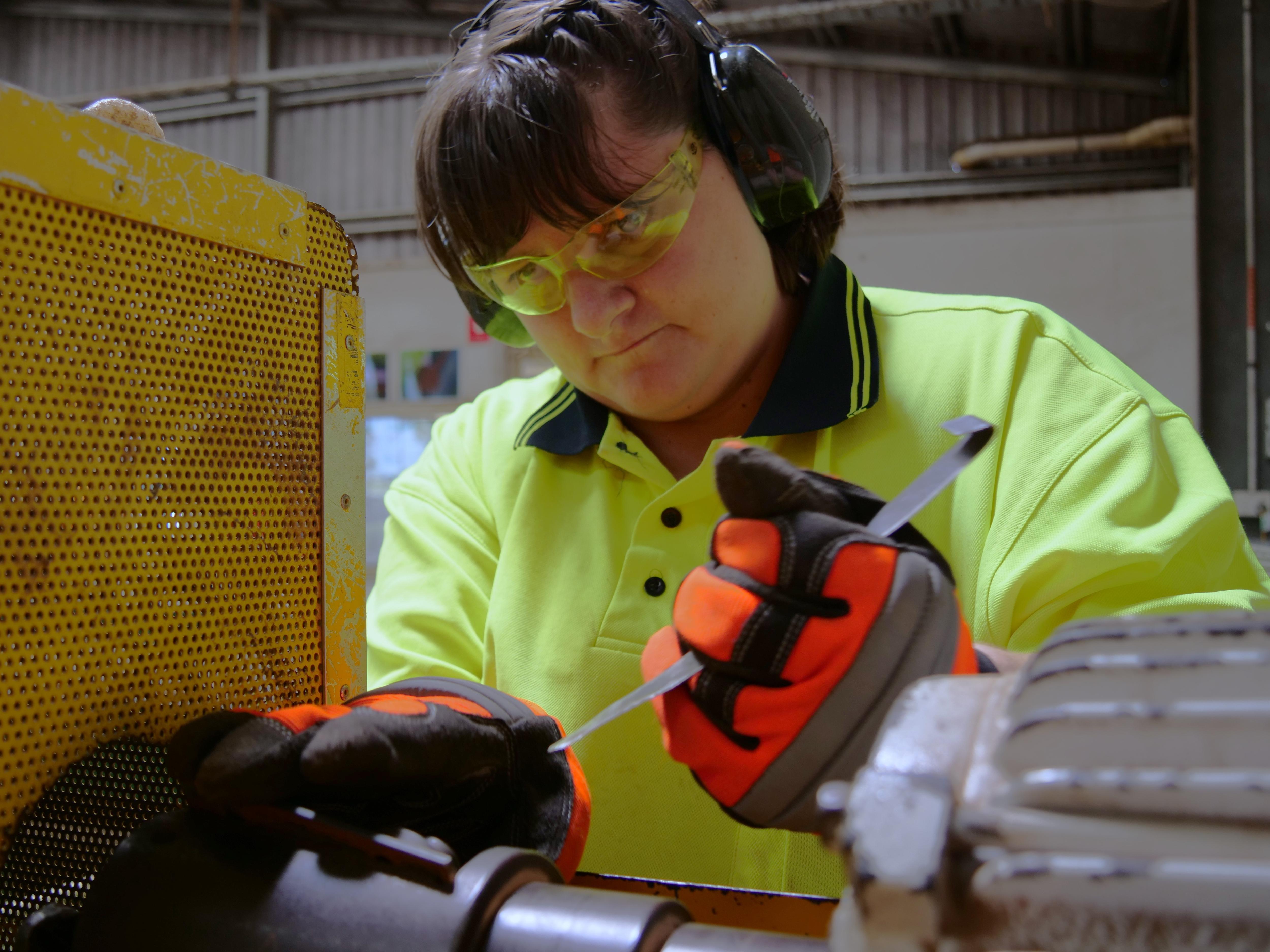 A woman in high visibility clothing works with tools. 