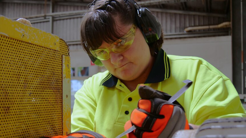 A woman in high visibility clothing works with tools. 