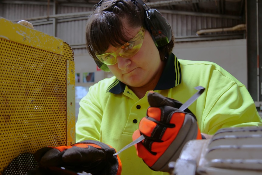 A woman in high visibility clothing works with tools. 