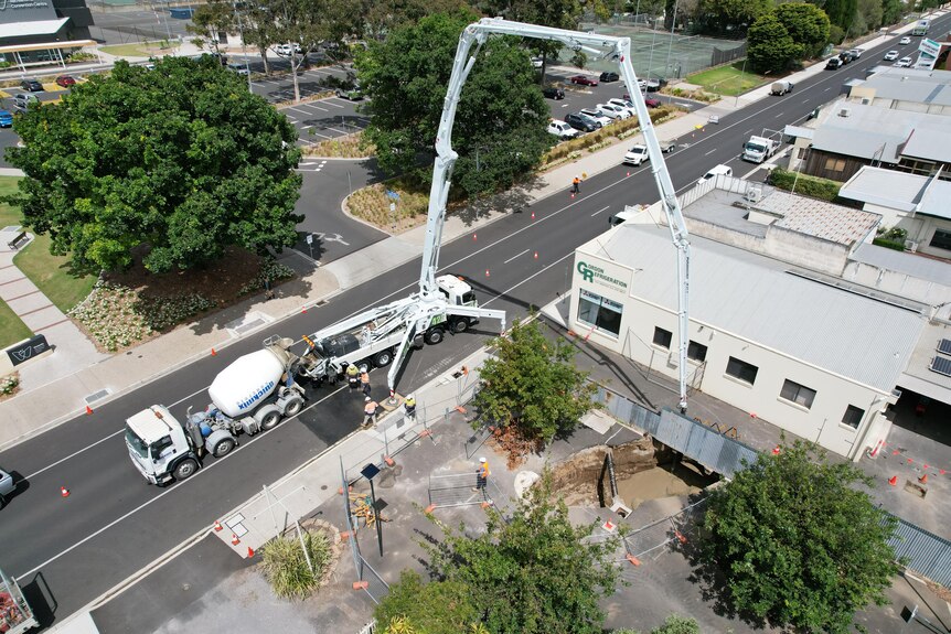 An aerial shot of a crane being used to pump filling into a large sinkhole.