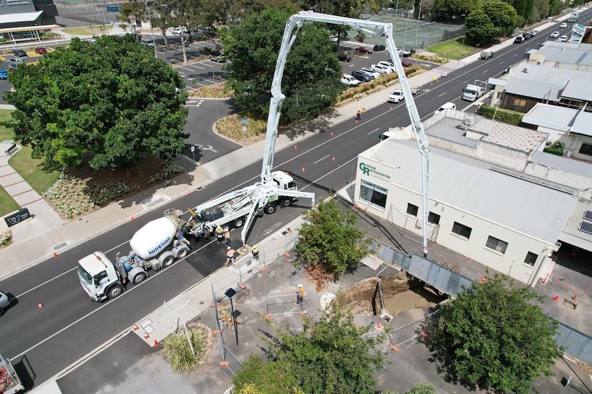 An aerial shot of a crane being used to pump filling into a large sinkhole.