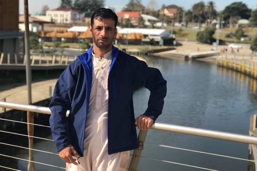 A man looks at the camera while leaning against a bridge rail.