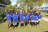 A group of students in school uniform, standing with their hands raised in the air.