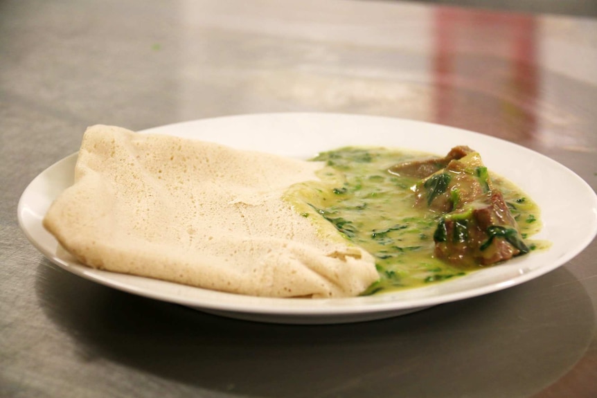 A plate of kombo, a traditional South Sudanese dish. It appears to consist of a flatbread, red meat and a green vegetable sauce.