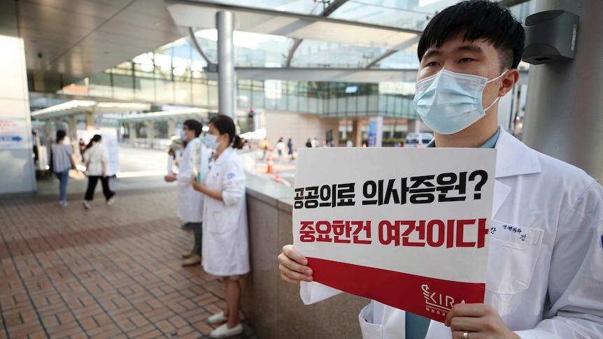 Doctors in coats and face masks hold signs in Korean saying: "Public medical doctor increase? What matters is the conditions."