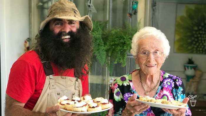 Man and elderly lady smiling at the camera and carrying plates of scones