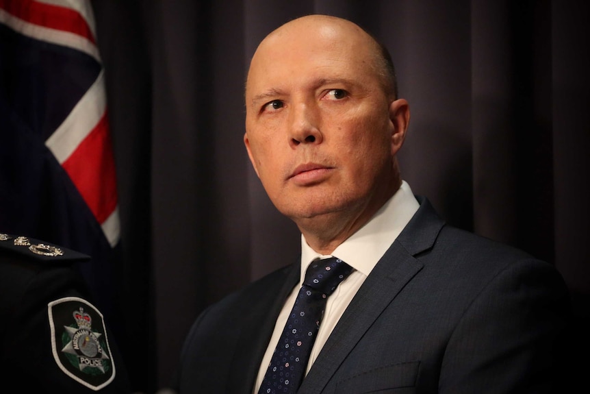 Dutton is wearing a dark suit, his eyes darting to the right of frame.