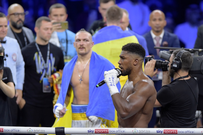 Anthony Joshua speaks on a microphone as men look on