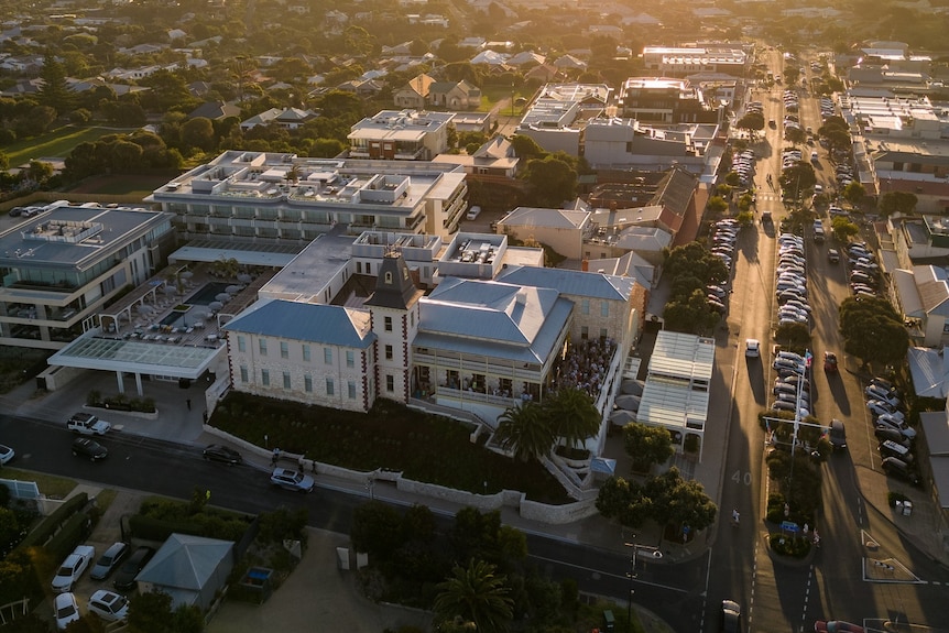 An aerial photo of a small, busy town at sunset with a hotel in the foreground and cars parked along the main street.