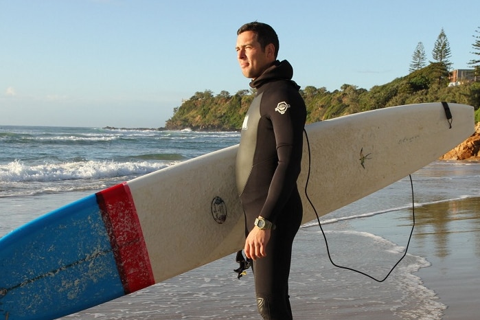 Man stands at beach holding surfboard