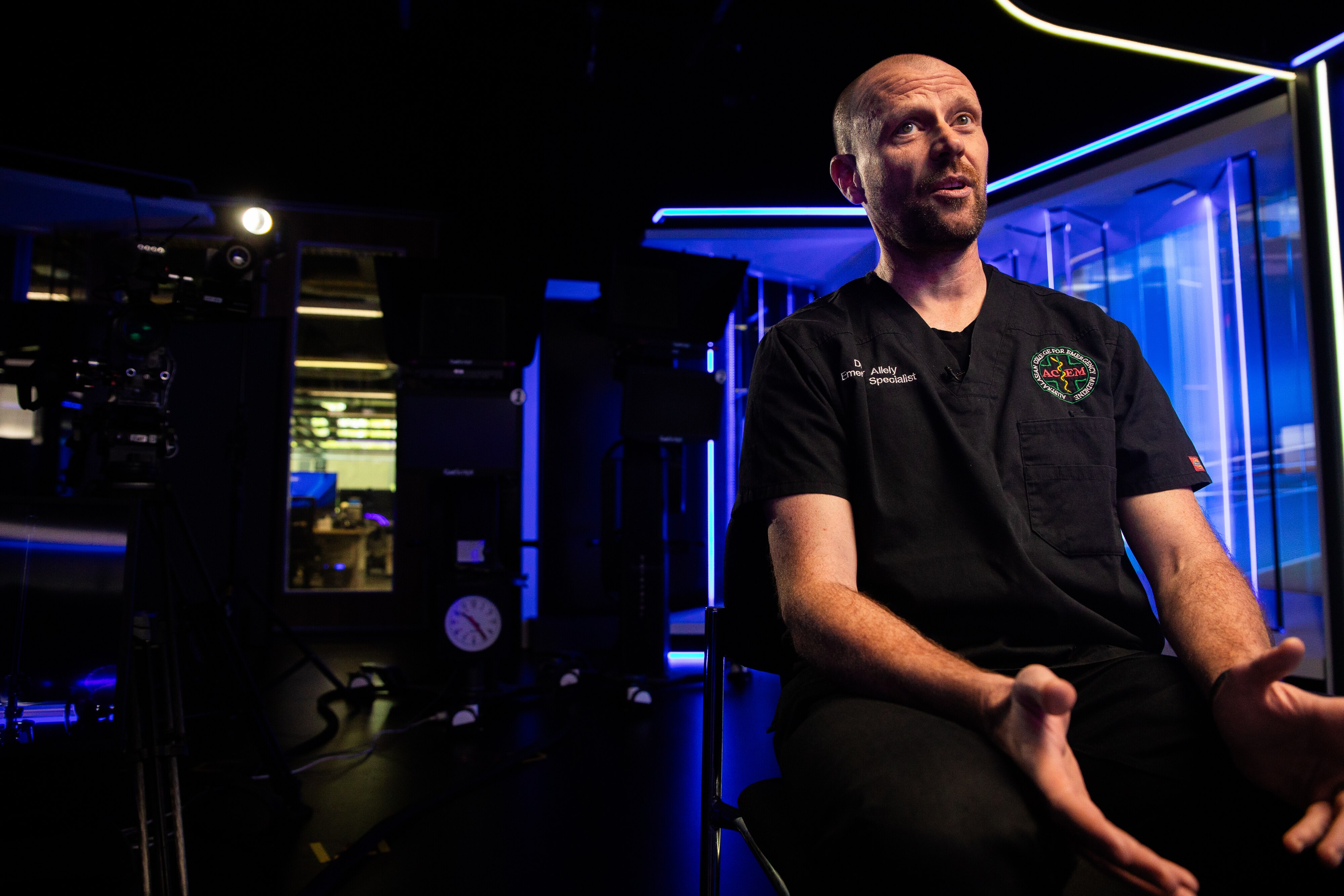 Peter Allely sits in a dark studio with blue lights behind.