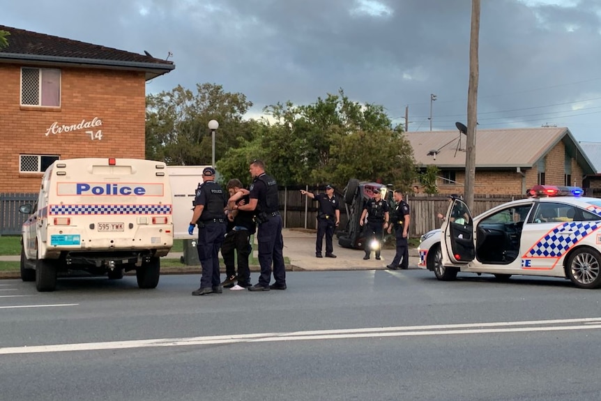 Two police cars outside a unit complex with officers handling a man and taking him to a paddywagon