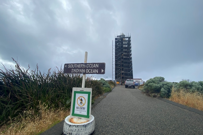 A wooden sign and a lighthouse covered in scaffolding